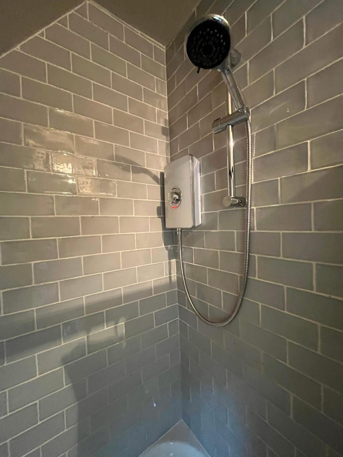 Electric shower fitted on grey metro-tiled wall